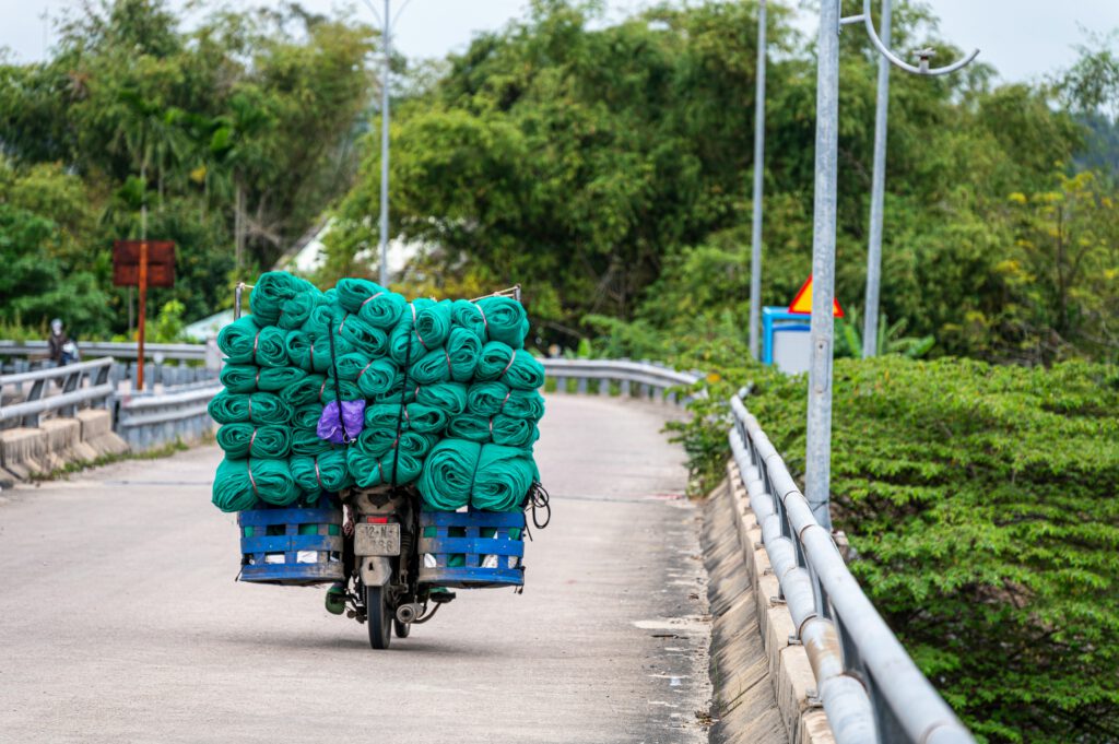 motorbike with lots of fisherman nets on the bag piled up high, driving on a road surrounded by nature