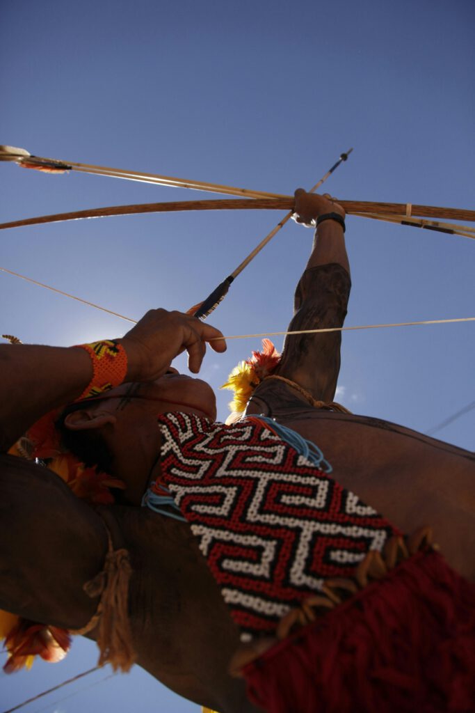 spiritua warrior, native indigenous man with indigenous scarf and wrist bands, holding an arrow how up int he sky, seen from below